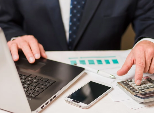 Businessman using a laptop and calculator with financial charts on the desk.